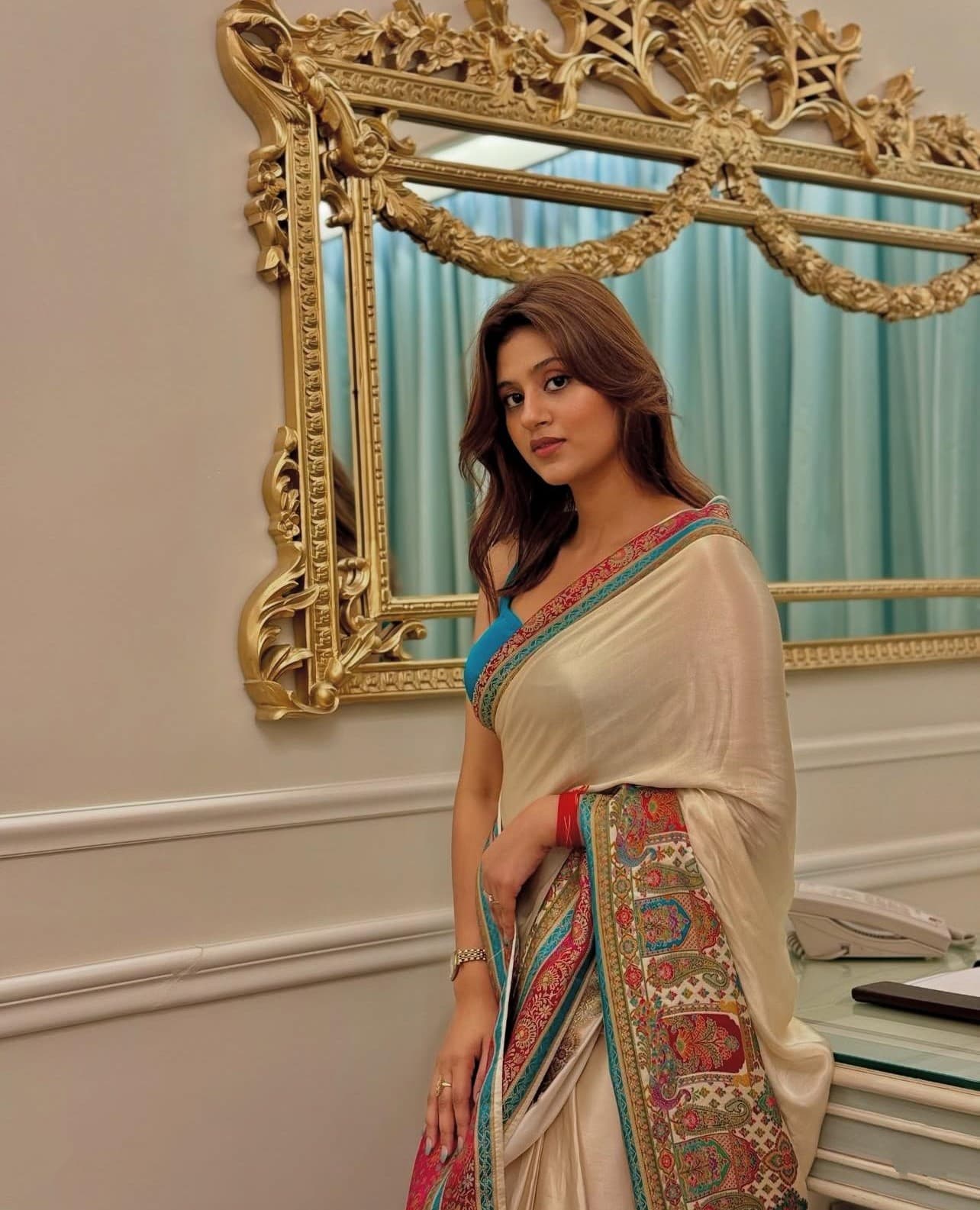 Woman in a saree standing in front of an ornate mirror