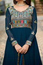 Woman wearing a dark blue dress with intricate colorful embroidery on a blurred outdoor background