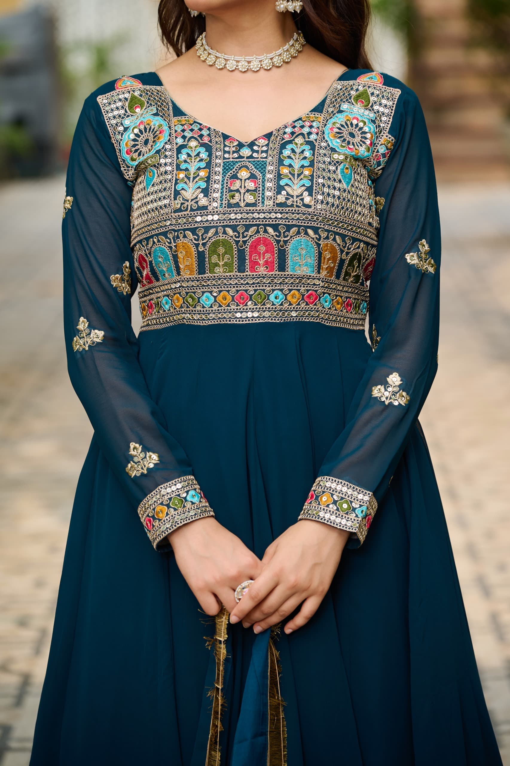 Woman wearing a dark blue dress with intricate colorful embroidery on a blurred outdoor background